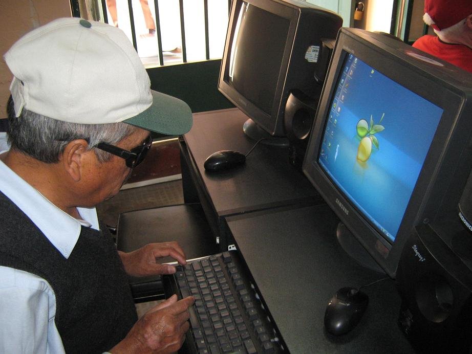 Persona con discapacidad visual posa sentado frente a una computadora.